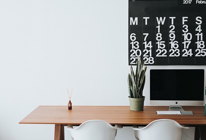 A tidy desk with a monitor and a wall calendar